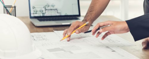 Architect or engineer team discussing a project design using blueprints and a laptop computer at the office before visiting work site.