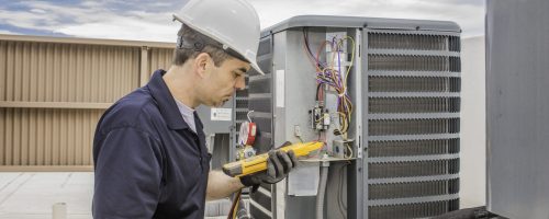 Trained hvac technician holding a voltage meter, performing preventative maintenance on a air conditioning condenser unit.