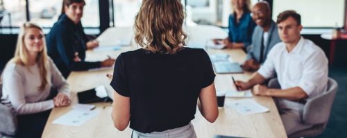 Rear view of a businesswoman addressing a meeting in office. Female manager having a meeting with her team in office boardroom.